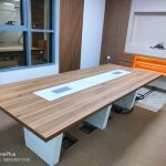Conference Desk top in wooden finish with white legs inside a conference room.